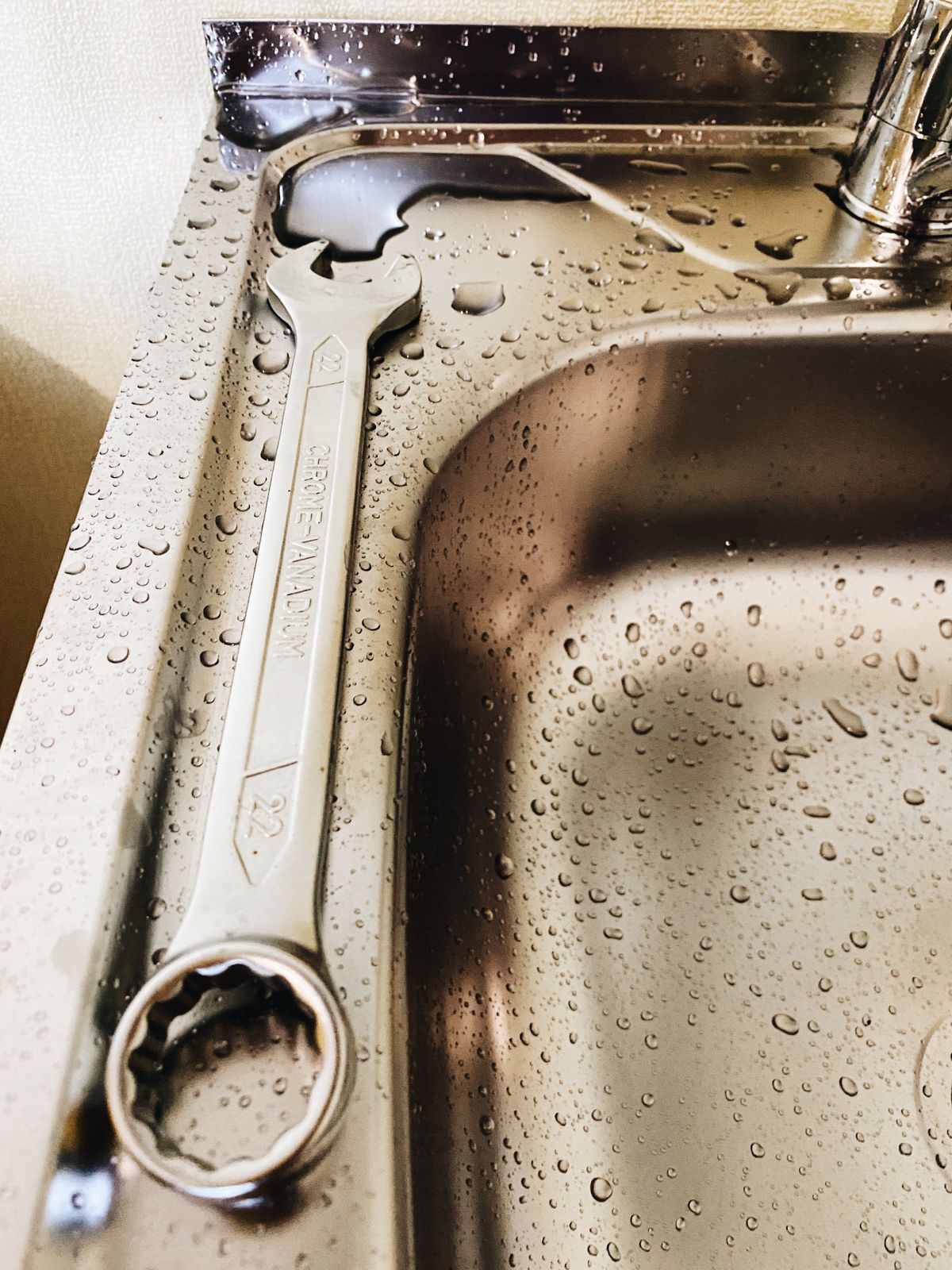 A wrench resting on a stainless steel sink during a repair